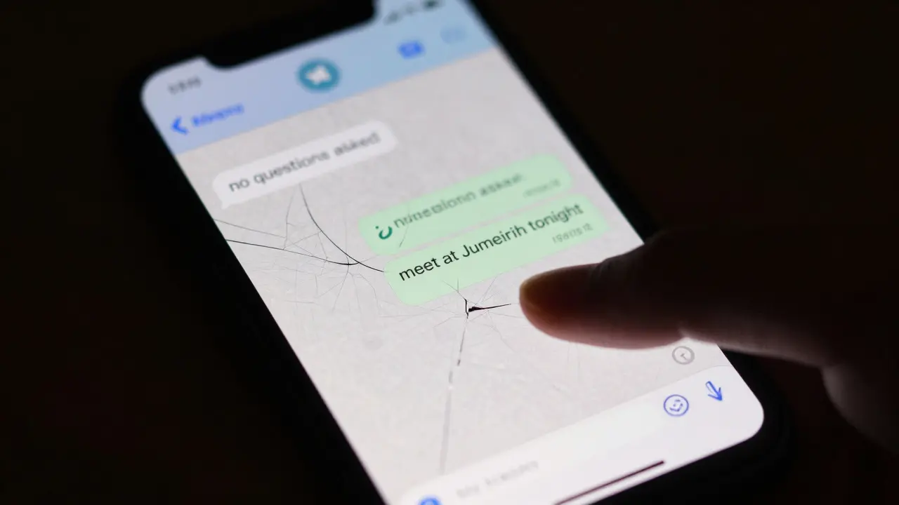 A cracked smartphone screen showing encrypted messages about a secret meeting in Dubai.