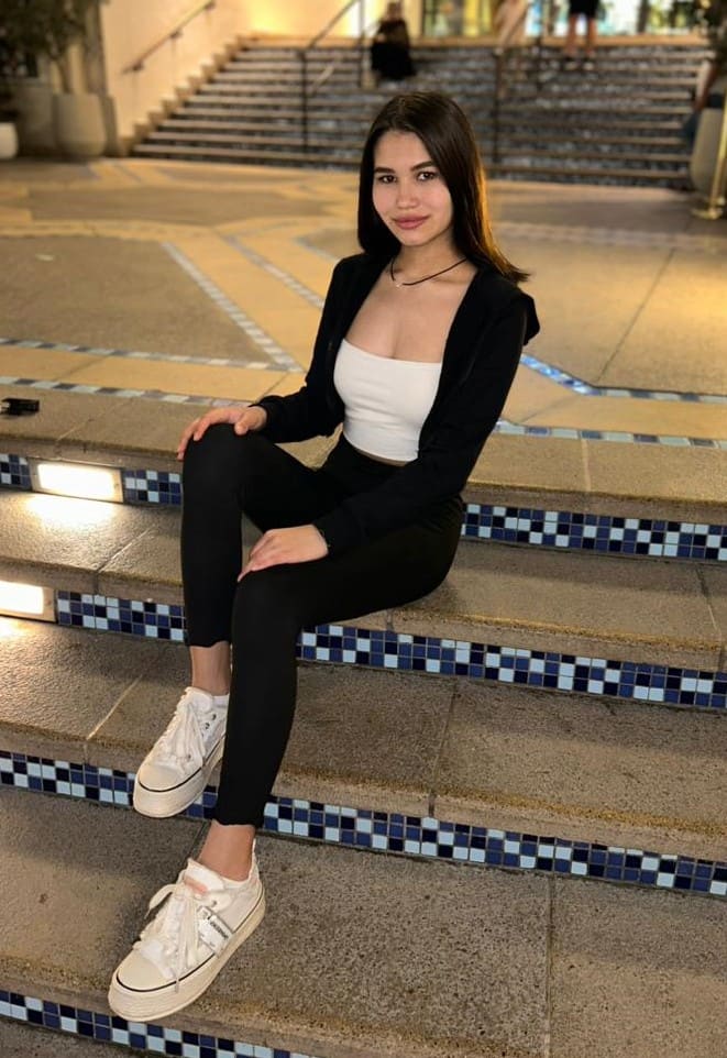 Woman sitting on outdoor steps in a white crop top, black cardigan, leggings, and platform sneakers, near planters.