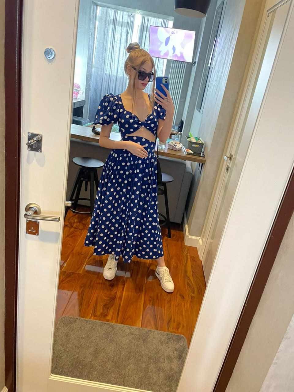 Mirror selfie in a blue and white polka-dot cropped top and long skirt, wearing white sneakers and sunglasses.