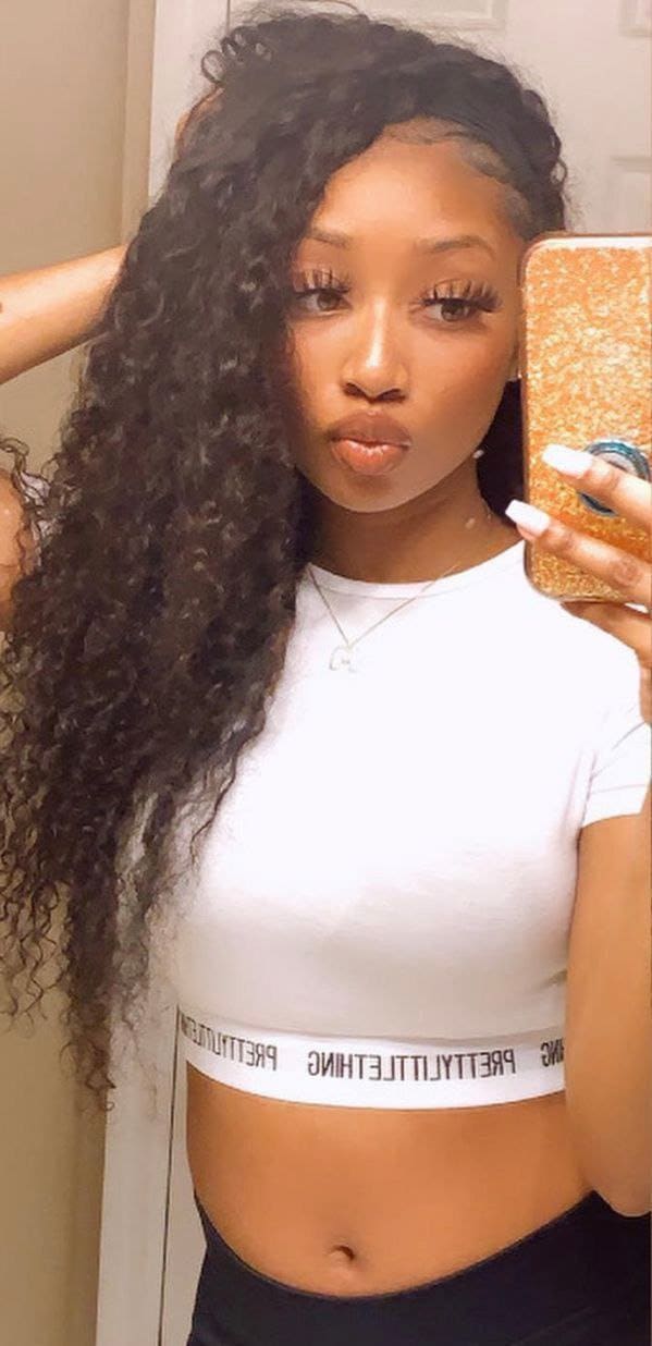 A mirror selfie shows a woman in a white cropped tee and dark bottoms holding a gold phone case indoors.