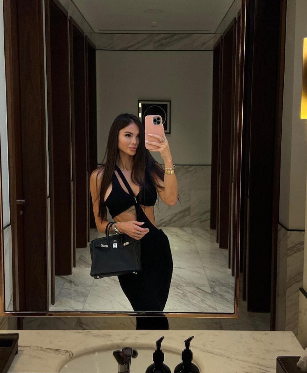Mirror selfie in a marble bathroom featuring a black cut-out halter top, high-waisted pants, and pink phone.